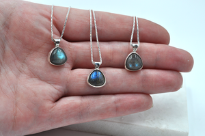 Three individual labradorite necklaces set in sterling silver shown in a hand to show size comparison as well as color variations of the stones.
