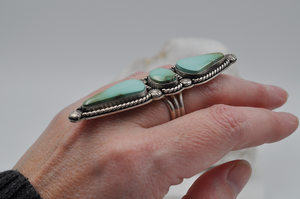 This large Royston turquoise ring features stones stones; one oval and two elongated teardrop shapes surrounded by sterling silver twisted rope and starburst ball embellishments in a satin finish. A side view of this statement ring is pictured here on a model. US Size 7.5